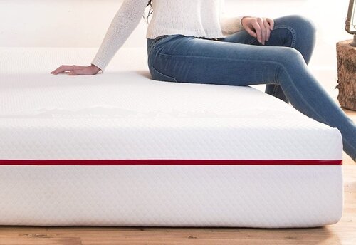 The best mattress in Canada page on www.themattressbuyerguide.com. Model sitting on edge of the Douglas Mattress