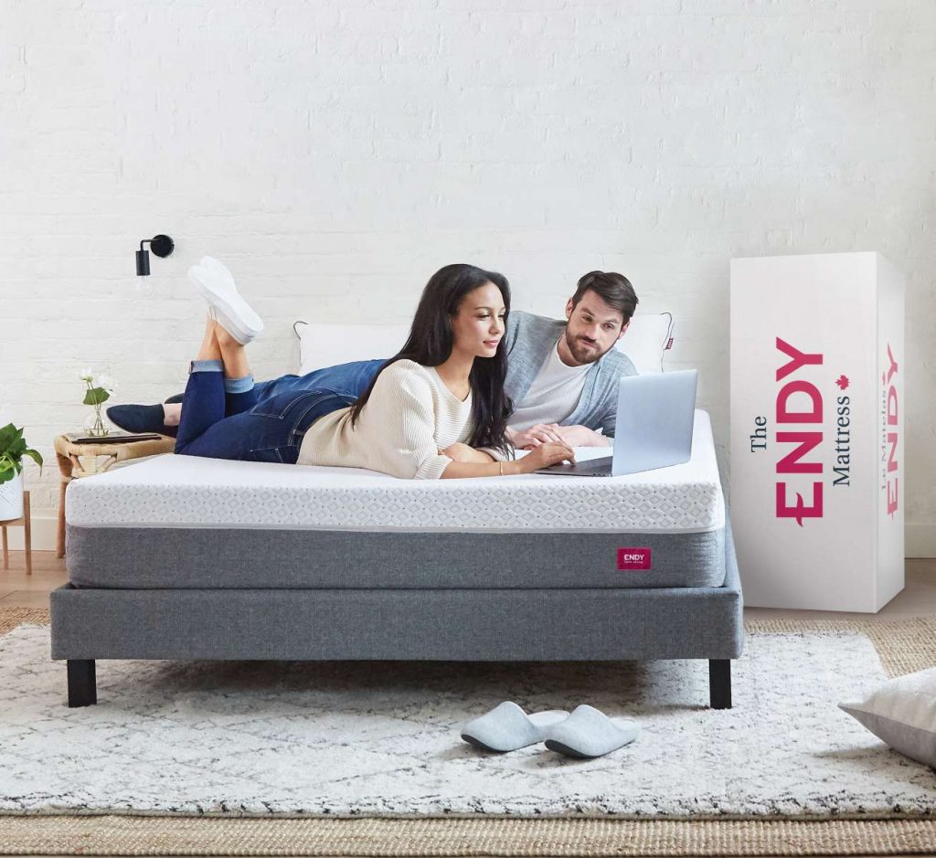 A couple is relaxing and working on a laptop while lying on the Endy Mattress