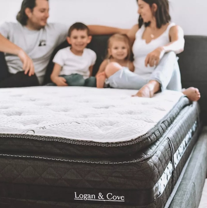 photo of a family of four sitting on a Logan And Cove mattress showing the depth of the pillow top section as well as suggesting overall comfort.
